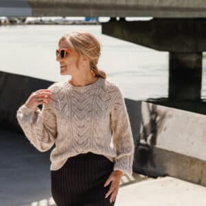Lady wearing the Cable Bay Sweater in pale natural tones.