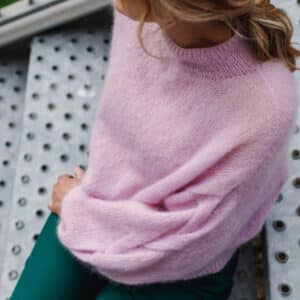 Woman sitting wearing pink knitted Plait sleeve knitted jumper